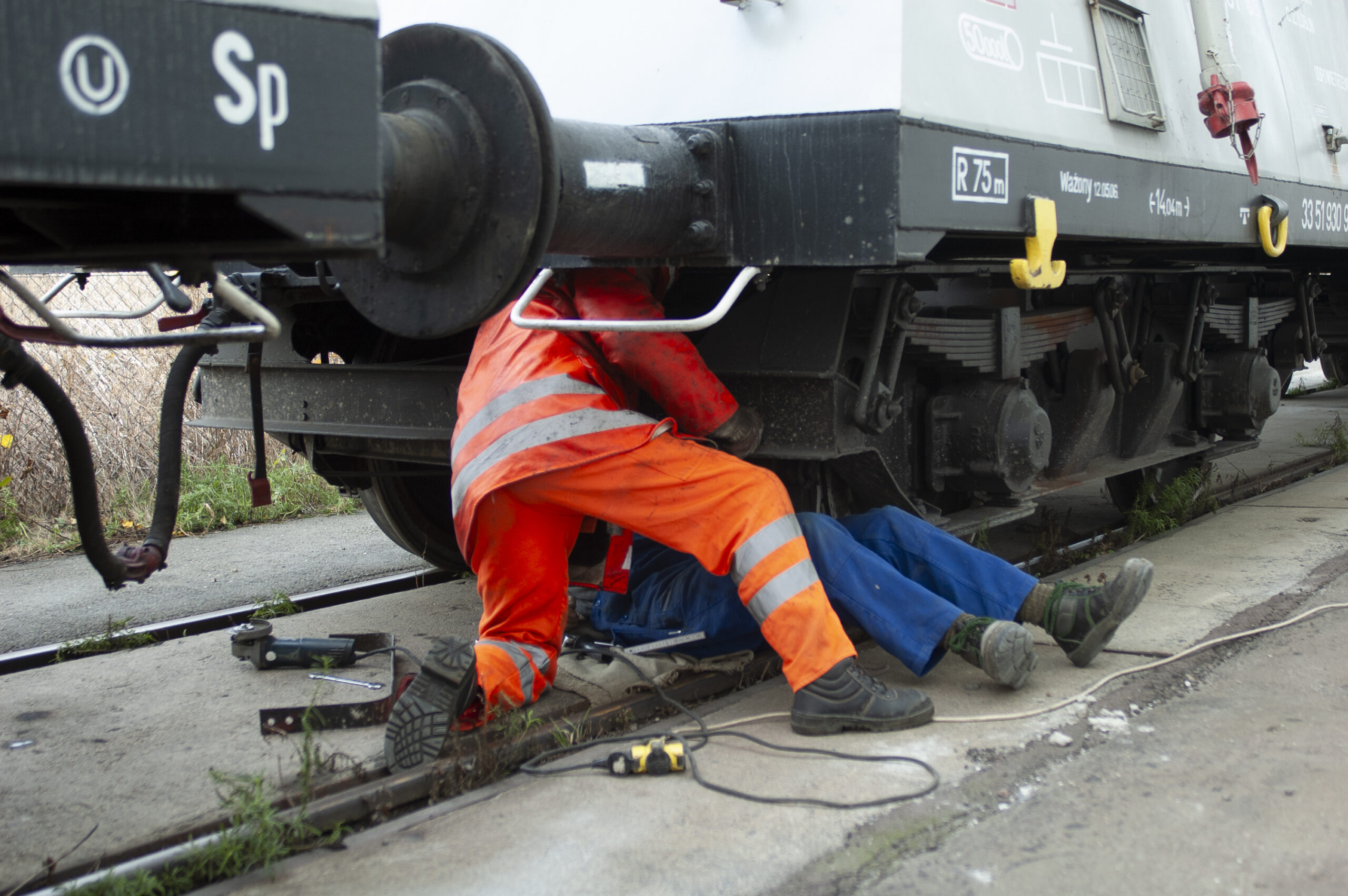 Zwei Personen in Arbeitskleidung arbeiten unter einem Güterwagen am Gleis